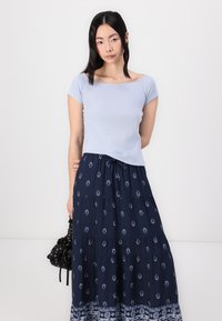 Top ajustado azul claro com mangas curtas, combinado com uma saia maxi azul marinho com padrões florais brancos e um design em camadas.