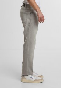 Pantaloni dritti grigio chiaro con una texture liscia, dotati di tasche standard, vita con passanti per la cintura e indossati con sneakers bianche.