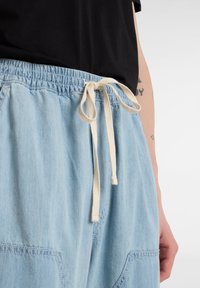 Ljusblå denimbyxor med elastisk midja och krämfärgad dragsko. Funktioner inkluderar framfickor och avslappnad passform.