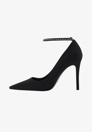 Zwarte high-heeled pump met puntige neus, van suède materiaal, enkelbandje versierd met kleine rhinestones en een strakke silhouette.