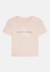 Vaaleanpunainen lyhythihainen t-paita, valmistettu puuvillasta; siinä on valkoinen "Calvin Klein Jeans" -logo ja nepparikiinnitys olkapäällä.