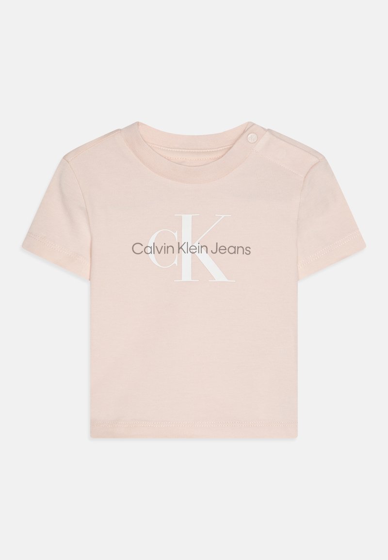 Vaaleanpunainen lyhythihainen t-paita, valmistettu puuvillasta; siinä on valkoinen "Calvin Klein Jeans" -logo ja nepparikiinnitys olkapäällä.