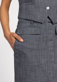 Blauwe textuurstof kleding met een getailleerd ontwerp, voorzien van twee voorzakken en een enkele knoopsluiting in de taille.