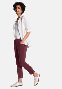 Lättvikts, långärmad vit blus över en åtsittande vit topp, tillsammans med bordeauxslim byxor och vita sneakers med grå detaljer.