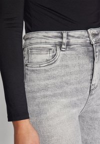 Grå högmidjade jeans med en urblekt design, utrustade med framfickor och dragkedja, kombinerade med en svart långärmad topp.