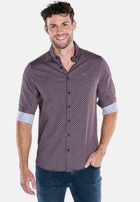 Herren-Hemd in Kastanienbraun mit einem geometrischen Muster. Es verfügt über kontrastierende hellblaue Manschetten an den aufgekrempelten Ärmeln und schwarze Knöpfe.