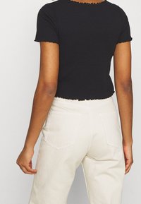 Haut noir côtelé à manches courtes avec encolure et ourlet festonnés, porté avec un pantalon taille haute blanc cassé doté de poches arrière.