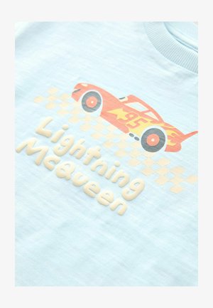 T-shirt azzurro chiaro con un'auto da corsa rossa con fiamme, sovrapposta al testo "Lightning McQueen" in lettere beige in rilievo.