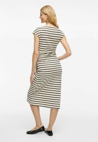 Pasiasta sukienka midi w kolorze beżowym i czarnym, z krótkimi rękawami, dopasowanym krojem, miękkiego materiału i bocznym rozcięciem. Noszona z czarnymi balerinkami.