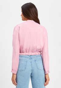 Lichtroze cropped jas met lange mouwen, elastische tailleband en een soepele stof; gecombineerd met lichtblauwe high-waisted jeans.