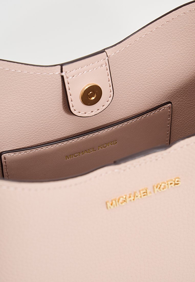 L'intérieur du sac à main en cuir rose présente un fermoir à pression doré, avec une poche visible et une marque embossée en doré. Texture lisse dans l'ensemble.