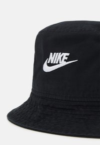 Crni šešir s raširenim rubom napravljen od pamučne tkanine s rebrastom teksturom. Sadrži bijeli izvezeni Nike logo sprijeda. Rašireni rub sa šivenim detaljima.