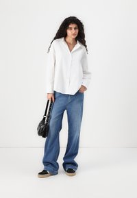 Valkoinen kauluspaita, yhdistettynä leveälahkeisiin sinisiin farkkuihin ja mustiin kenkiin. Asusteena pieni musta laukku.