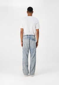 Λευκό κοντομάνικο μπλουζάκι και ανοιχτό μπλε, φαρδιά τζιν παντελόνια με ελαστική μέση και πλαϊνές λεπτομέρειες, που φαίνονται από πίσω.