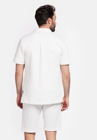 Witte polo met korte mouwen en een relaxte pasvorm, gecombineerd met witte shorts met opgerolde mouwen. Gladde stof met een schoon, minimalistisch ontwerp.