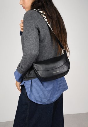 Bolso cruzado de cuero negro con superficie texturizada, con forma curva y una correa con patrón. Logo visible en el frente.