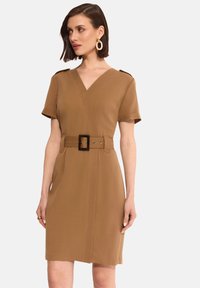Beżowa sukienka z paskiem, dekoltem w literę V, krótkimi rękawami i akcentami na ramionach. Posiada pionowe przeszycia i wykonana jest z gładkiego materiału.