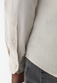 Beiges Langarmhemd mit schlankem Schnitt, mit Knopfmanschetten und klassischem Kragen. Der Stoff hat eine glatte Textur und einen dezenten Glanz.