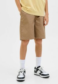 Shorts marron en tissu tissé, longueur genou, avec une coupe droite. Portés avec des chaussettes blanches et des baskets noir et blanc.