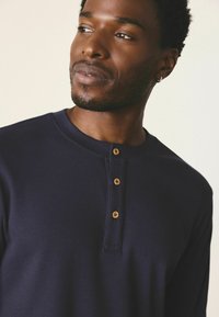 Navy gestreiftes Langarmshirt mit Rundhalsausschnitt, das eine Knopfleiste mit Holzknöpfen und eine weiche Textur bietet.