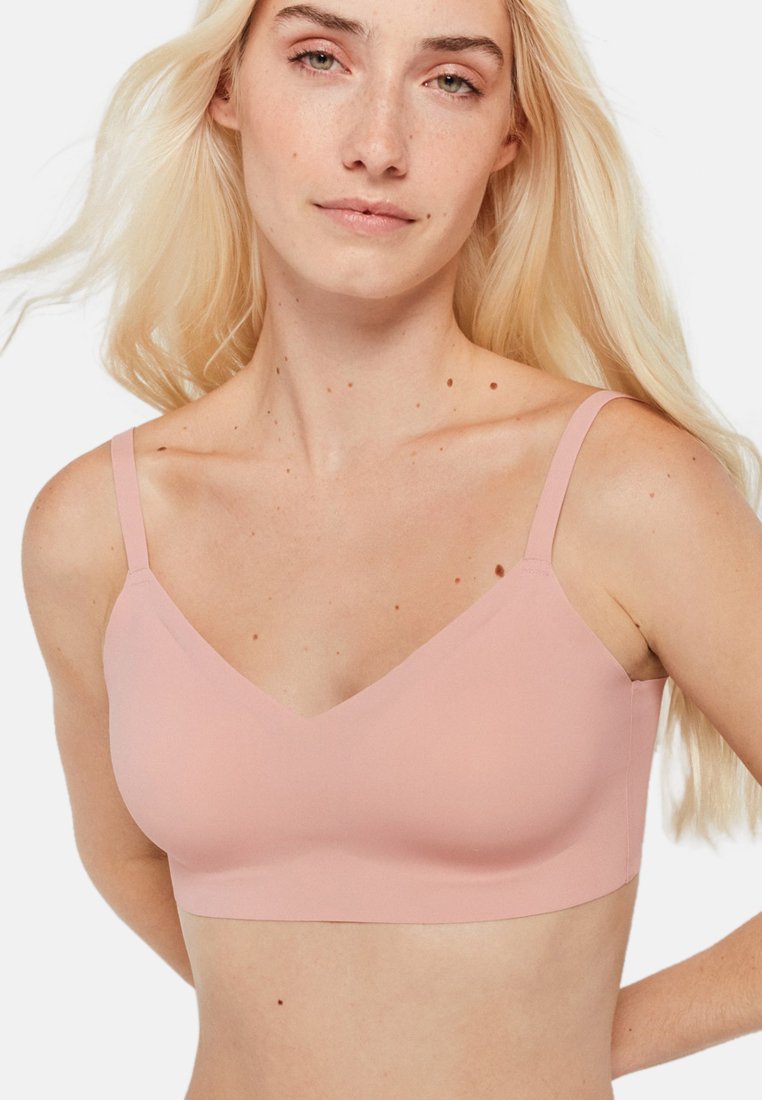 Bralette rose clair avec un décolleté en V, des bretelles réglables, une texture lisse et sans fermetures visibles ni rembourrage. Design simple et minimaliste.