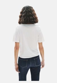 Witte shirt met korte mouwen, een ronde hals, een zachte textuur en een relaxte pasvorm, gecombineerd met donkerblauwe jeans.