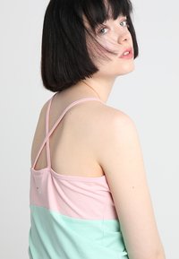 Tank topp i rosa og mint-fargeblokk med justerbare krysse-stropper, myk stoff og logo-detalj på baksiden.