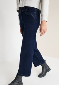 Marineblauwe wijde jeans van een soepele denimtextuur, met contrasterende stiksels en zakken, gecombineerd met zwarte veterschoenen.