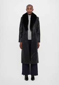 Μαύρο δερμάτινο παλτό με ψεύτικη γούνα στην γιακά, διπλό μπροστινό κλείσιμο, μακριά μανίκια και ίσια γραμμή, συνδυασμένο με γκρι μπλούζα και ναυτικές παντελόνες.