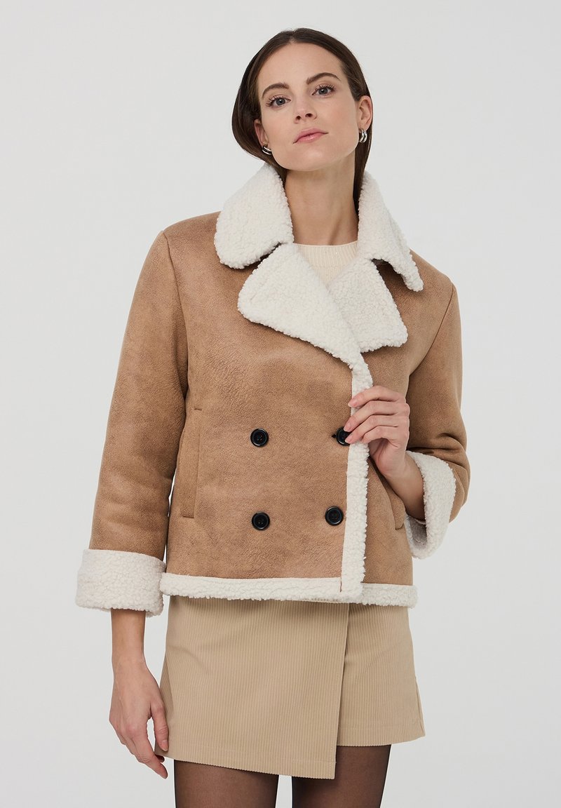 Giacca in shearling marrone doppiopetto con colletto e polsini bianchi; presenta bottoni neri e una texture morbida.