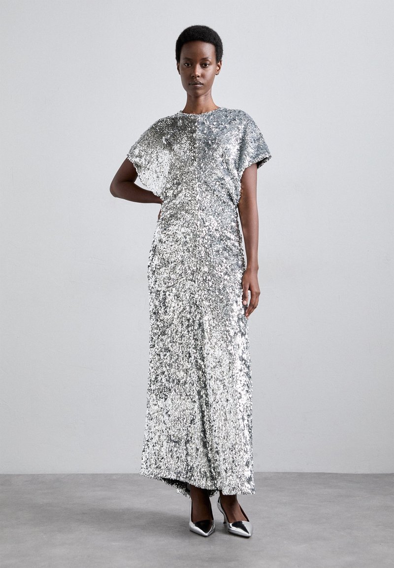 Silver sequin gown with short sleeves, floor-length design, and a straight silhouette. Paired with pointed black heels. Textured, reflective surface.
