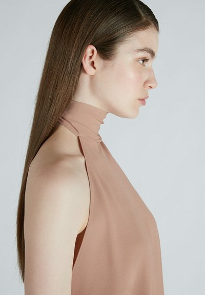 Top halter elegante in morbido tessuto color marrone chiaro con collo alto e lati aperti, caratterizzato da una texture liscia e dettagli minimi.