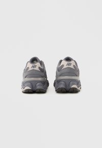 Gray athletic shoes with a textured mesh upper, cushioned sole, and contrasting beige accents. Features a curved design for added support.