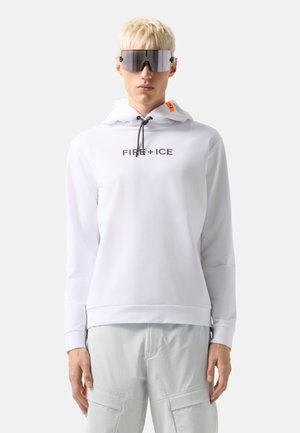Persoon met blond haar draagt grote spiegelende zonnebril, een witte hoodie met de tekst "FIRE + ICE" en lichtgrijze cargobroek tegen een effen achtergrond.
