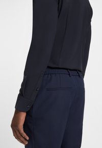 Navy Hemd mit langen Ärmeln, Knopfmanschetten und glatter Textur, kombiniert mit navyfarbener Hose mit strukturierter Oberfläche und elastischem Bund.