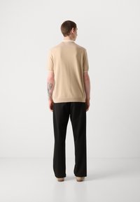 Μπεζ πλέκτο πόλο μπλουζάκι με κοντά μανίκια και ραβδωτό γιακά. Συνδυασμένο με μαύρα παντελόνια σε φαρδιά γραμμή. Λειαστή υφή, καθημερινή εφαρμογή.