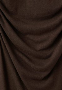 Tessuto di maglia marrone con una texture drappeggiata, caratterizzato da punti morbidi e uniformi e da una lucentezza sottile, che crea pieghe ondulate.