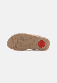 FitFlop sandal såle i beige gummi, med et teksturert mønster, preget merkevare og en sirkulær rød detalj. Jevn overflate generelt.