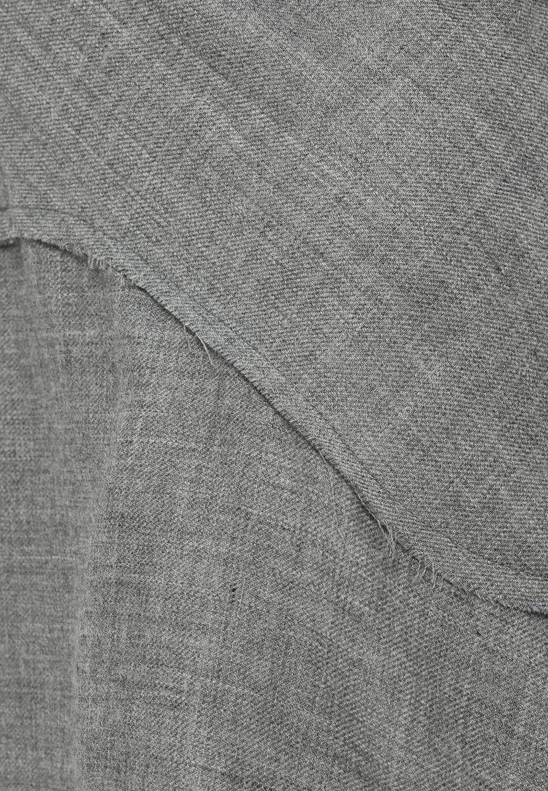 Gros plan sur un tissu gris avec des coutures visibles et des bords superposés montrant des détails de texture et de tissage.
