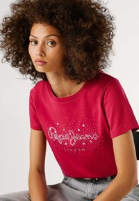 Rode katoenen t-shirt met een grafisch ontwerp met witte accenten waarop "London" staat. Korte mouwen en een ronde halslijn. Eenvoudige textuur.