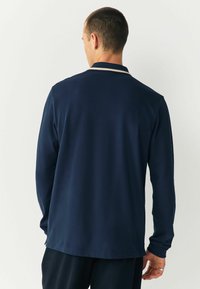 Marineblaues Langarm-Polohemd mit einem flachen Kragen, kontrastierendem Streifen am Kragenrand und einer weichen, glatten Textur. Verfügt über eine lockere Passform.