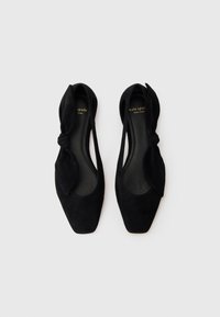 Black suede flats with a pointed toe and knotted bow detail on the side. Smooth interior with a branded insole.