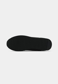 Black rubber sneaker sole with textured ridges for grip. Smooth surface with a rounded toe and slight heel. Minimalist design, no visible branding.
