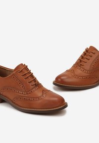 Chaussures oxford en cuir brun avec des perforations, bout arrondi et fermeture à lacets. Présente une finition lisse et une semelle contrastante.