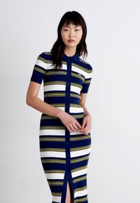 Adīta kleita ar īsām piedurknēm, kurai ir tumši zila, balta un dzeltena svītra. Tai ir pogātā priekšpuse un sānu šķirba papildu detaļai.