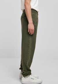 Olivegrønne sweats med elastisk talje, sidelommer og en afslappet pasform, parret med hvide sneakers med grønne detaljer.