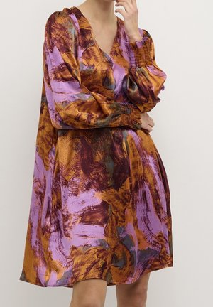 Woman wearing a loose, long-sleeve dress with abstract brushstroke print in purple, rust orange, and dark brown tones.
