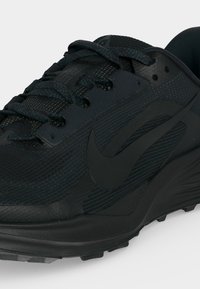 Chaussure de sport noire avec empeigne texturée, logo Swoosh noir et lacets noirs à motif sur fond blanc.