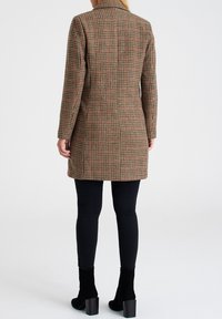 Brun rutig kappa med skräddarsydd passform, har en notched krage och långa ärmar, kombinerad med svarta åtsittande byxor och högklackade stövlar.
