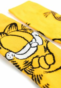 Calzini gialli con un design di un gatto cartoon in bianco e nero. Texture liscia con caratteristiche facciali e zampette ben definite illustrate sul tessuto.